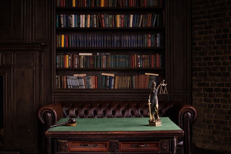 Mesa de escritório de advocacia com estatueta da justiça, poltrona de couro e estante de livros