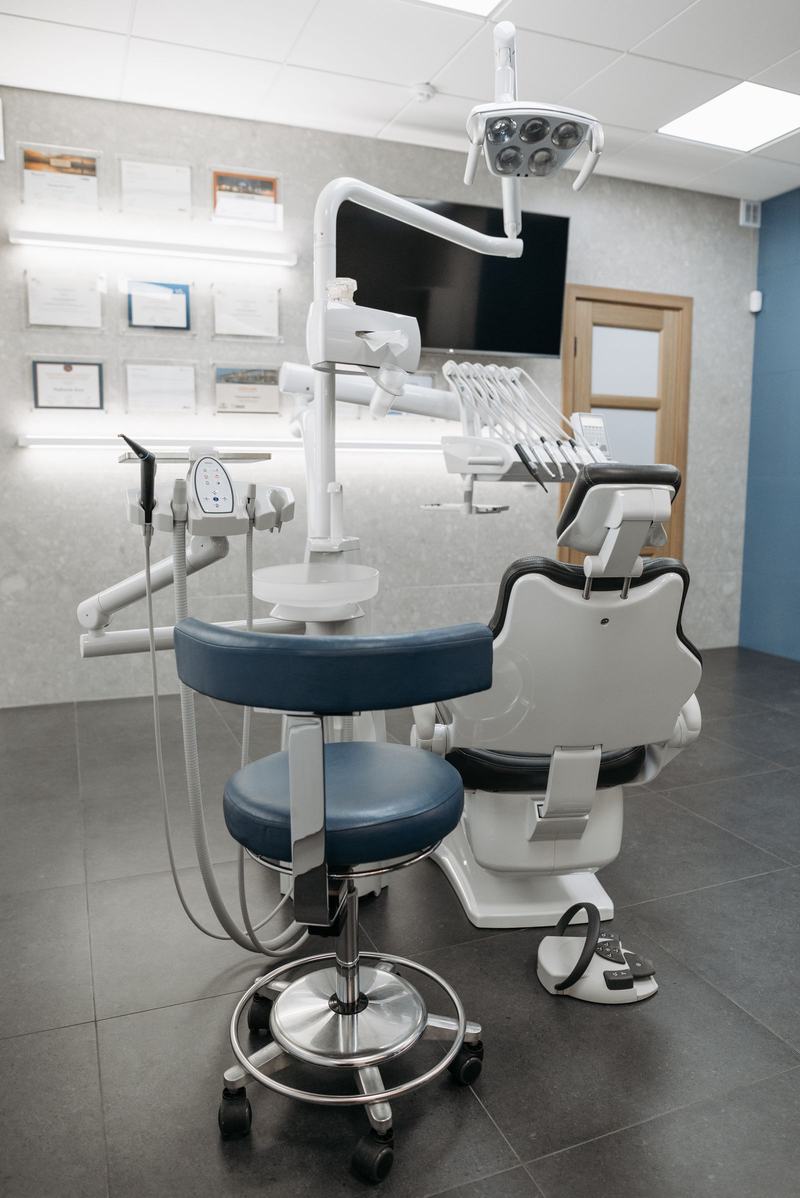 Sala de atendimento odontológico vazia, com cadeira azul e armários
