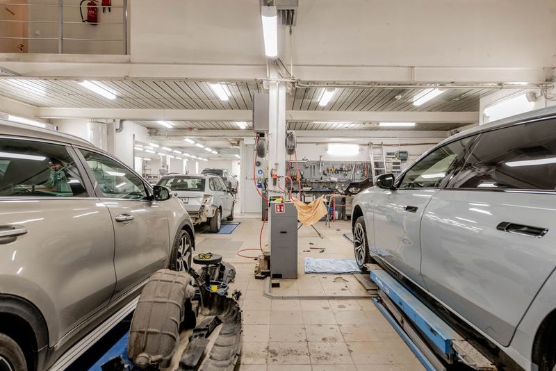 Interior de uma oficina mecânica clara, com dois carros nos elevadores e bancadas ao fundo
