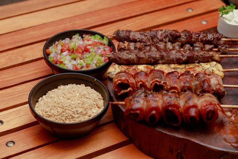 Espetos de carne com farofa e vinagrete sobre uma tábua de madeira