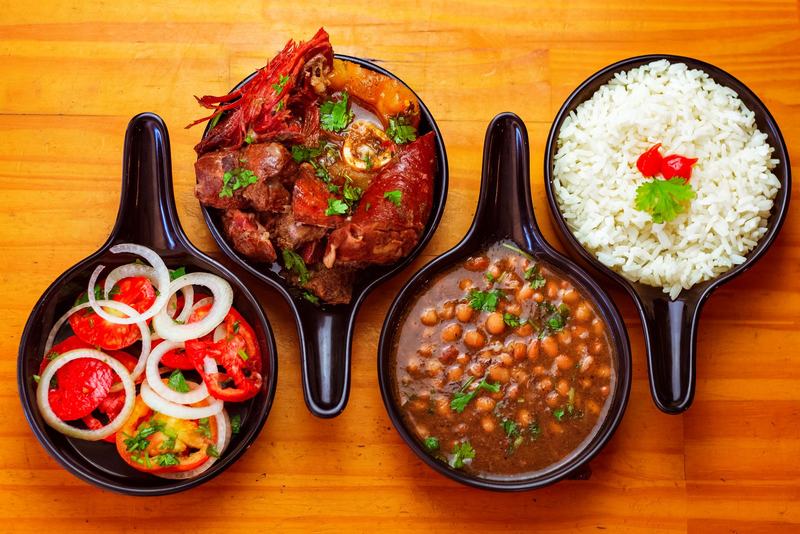 Panelas de ferro com carne, feijão, arroz e salada sobre uma mesa de madeira